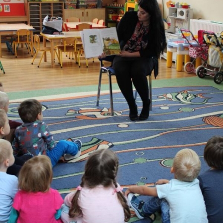 Bibliotekarka czyta książkę przedszkolakom. Pokazuje przy tym ilustracje. 