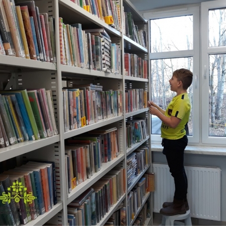 Chłopiec wyszkuje podaną książkę w bibliotecznym księgozbiorze. 