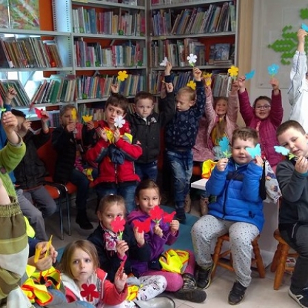 Dzieci pozują do zdjęcia w pomieszczeniu breńskiej biblioteki. Trzymają  motylki i kwiaty z papieru kolorowego. 