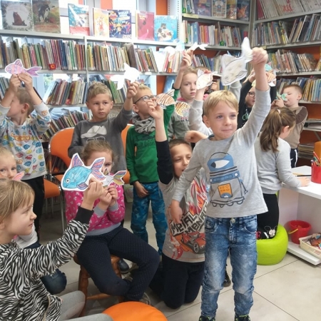 Dzieci pozują do zdjęcia w breńskiej bibliotece. Każdy z nich trzyma w ręku rybę z papieru. 