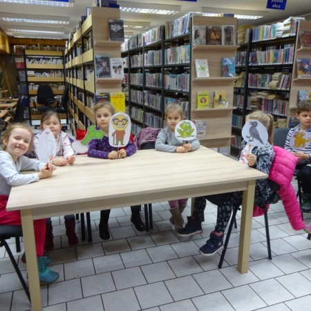 Grupa przedszkolaków siedzi przy stole. Dzieci trzymają ilsutracje postaci występujących w "Rzepce". 
