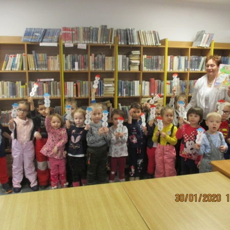 Dyrektor Janina Herzyk wraz z grupą przedszkolaków trzymają wykonane przez siebie bałwanki na patyku. Zdjęcie wykonane w pomieszczeniu magazynowym biblioteki w Brennej. 