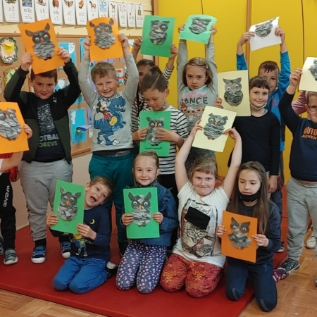 Fotografia kolorowa. Bibliotekarka pozuje do zdjęcia z dziećmi, które wykonały sowę - bohaterkę przedstawionej baśni.