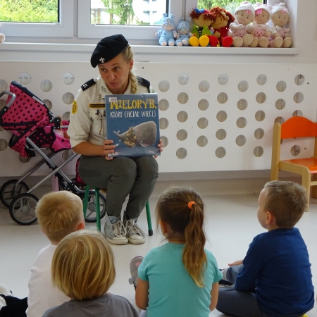 Fotografia kolorowa. Harcerka czyta dzieciom bajkę. 
