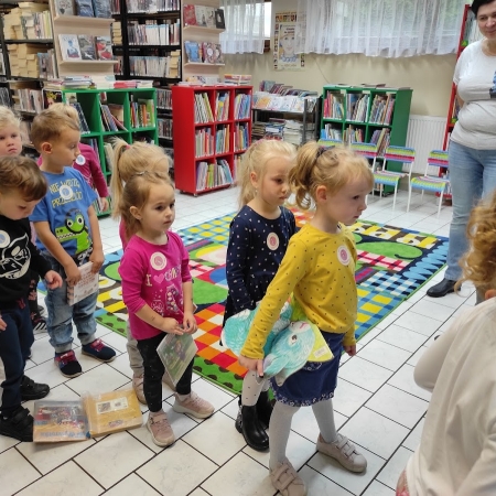 Fotografia kolorowa. Grupa przedszkolaków czeka na swoją kolej w wypożyczaniu książek. 