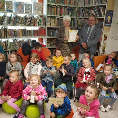 Fotografia grupowa seniorów i dzieci w bibliotece.