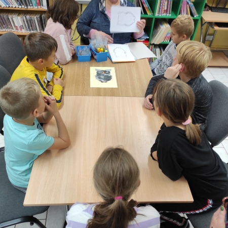 Fotografia kolorowa. Bibliotekarka tłumaczy dzieciom jak wykonać sowę z opowieści. 