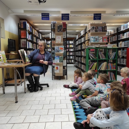 Fotografia kolorowa. Bibliotekarka czyta dzieciom bajkę. 