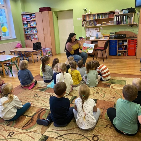 Fotografia kolorowa. Bibliotekarka czyta dzieciom bajkę. 