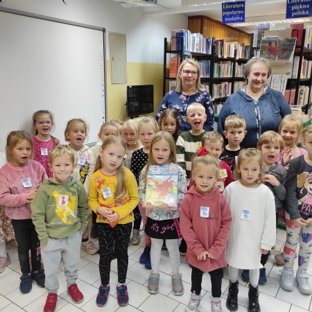 Fotografia kolorowa. Dzieci wraz z nauczycielką i bibliotekarką pozują do zdjęcia grupowego. 