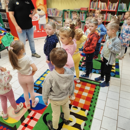  Fotografia kolorowa.  Zdjęcie grupowe przedszkolaków w pomieszczeniu biblioteki.