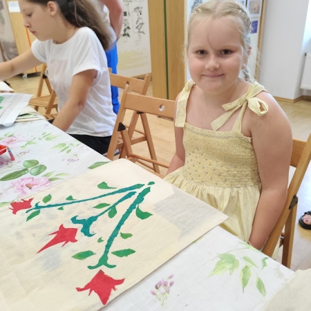 Fotografia kolorowa. Dziewczynka pozuje do zdjęcia ze swoją pracą plastyczną.