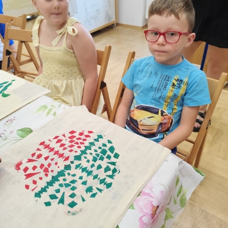 Fotografia kolorowa. Chłopiec pozuje do zdjęcia ze swoją pracą plastyczną.