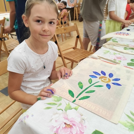 Fotografia kolorowa. Dziewczynka pozuje do zdjęcia ze swoją pracą plastyczną.