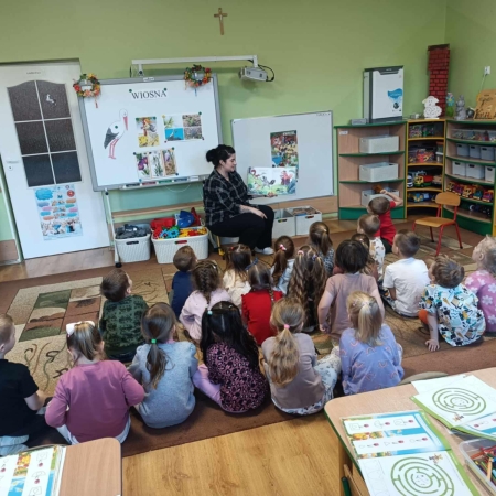 Fotografia kolorowa. Bibliotekarka czyta dzieciom bajkę w przedszkolu.