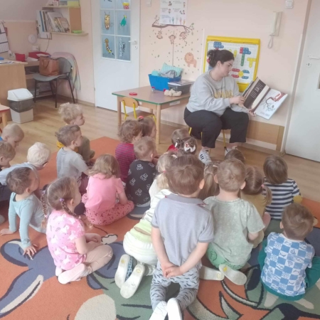 Fotografia kolorowa. Bibliotekarka czyta dzieciom bajkę. 