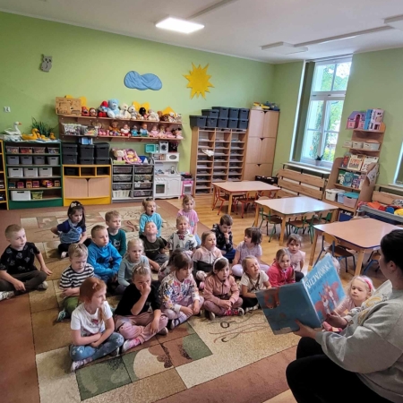 Fotografia kolorowa. Bibliotekarka czyta dzieciom bajkę. 