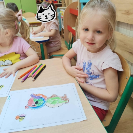 Fotografia kolorowa. Dziewczynka i jej praca plastyczna.