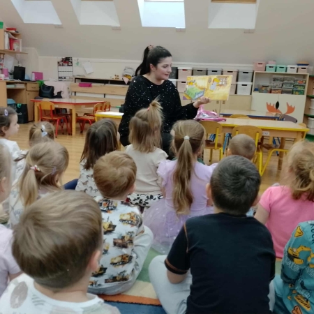 Fotografia kolorowa. Bibliotekarka czyta dzieciom opowiadanie o Kubusiu Puchatku.