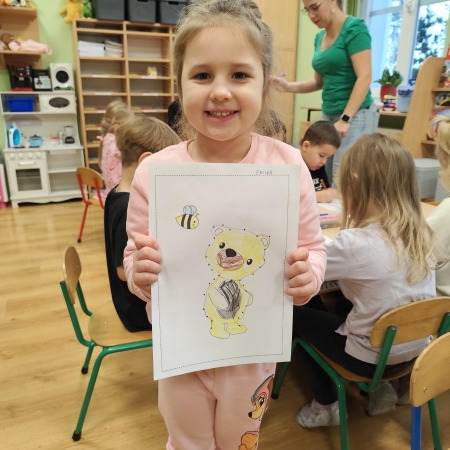 Fotografia kolorowa. Dziewczynka i jej praca plastyczna.