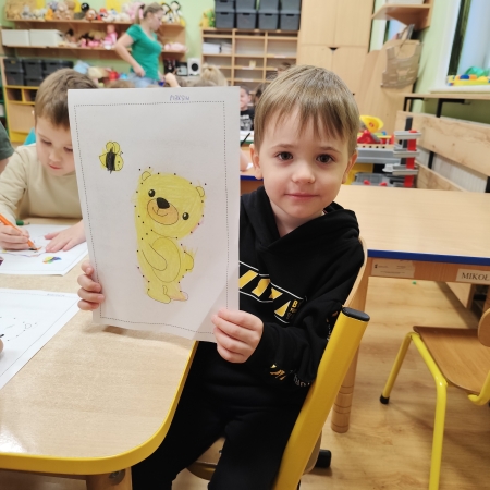 Fotografia kolorowa. Chłopiec i jego praca plastyczna.