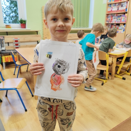 Fotografia kolorowa. Chłopiec i jego praca plastyczna.