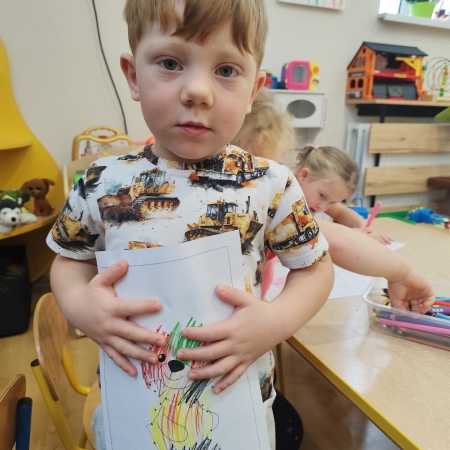 Fotografia kolorowa. Chłopiec i jego praca plastyczna.