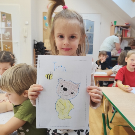 Fotografia kolorowa. Dziewczynka i jej praca plastyczna.