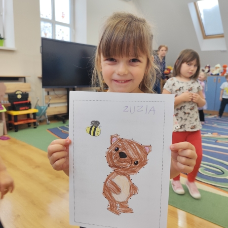 Fotografia kolorowa. Dziewczynka i jej praca plastyczna.