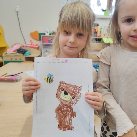 Fotografia kolorowa. Dziewczynka i jej praca plastyczna.