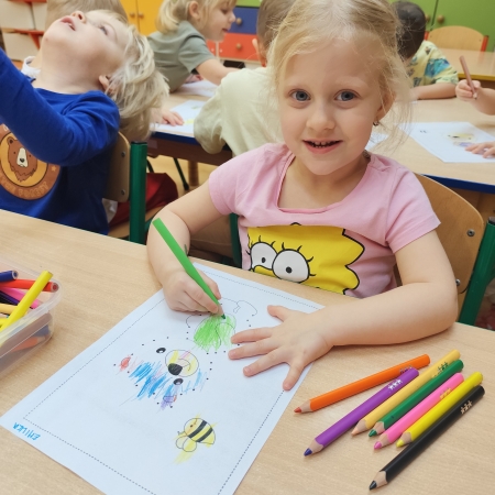 Fotografia kolorowa. Dziewczynka i jej praca plastyczna.