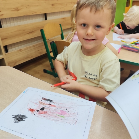 Fotografia kolorowa. Chłopiec i jego praca plastyczna.