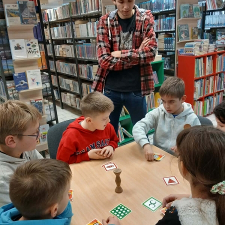 Fotografia kolorowa. Uczestnicy mikołajkowego planszogrania we wnętrzu filii w Górkach Małych.