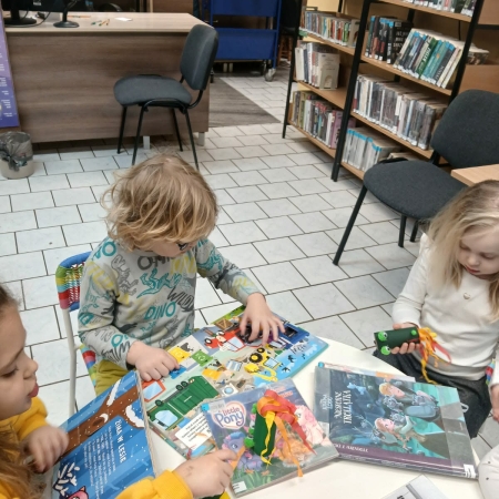 Fotografia kolorowa. Przedszkolaki przeglądają książki w bibliotece w Górkach Małych. 