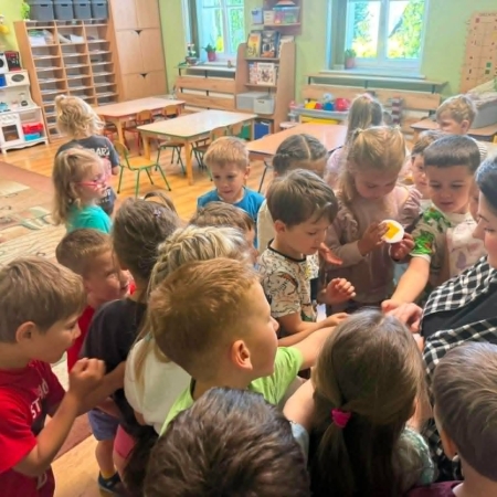 Fotografia kolorowa. Grupa przedszkolaków otrzymuje od bibliotekarki odznaki ze spotkania z napisem "Kocham pszczoły". 